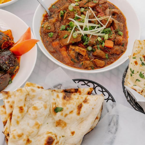 Indian lamb curry with ginger and scallions, eggplant, and naan bread on a white tablecloth.