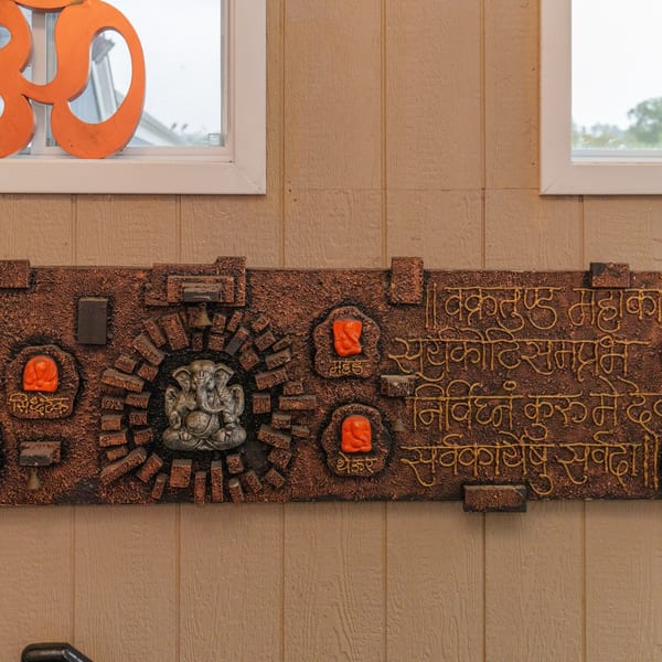Indian wall art with a Ganesha statue, orange accents, and Sanskrit text on a textured brown background.