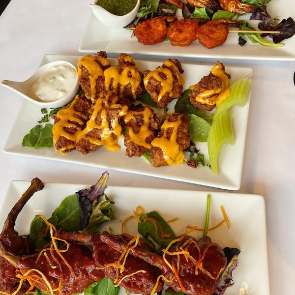 Three plates of Indian appetizers: chicken pakora, shrimp skewers, and roasted duck, with sauces.