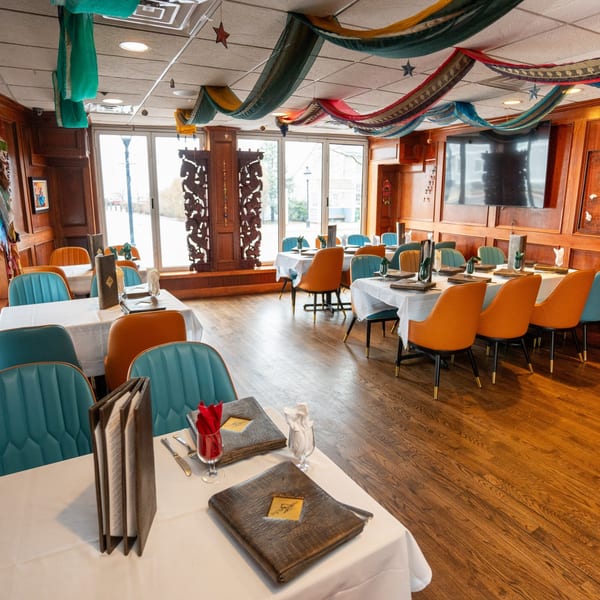 Curry Club dining room with teal and orange chairs, white tablecloths, and colorful ceiling drapes.