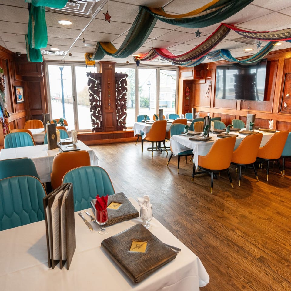Curry Club dining room with teal and orange chairs, white tablecloths, and colorful ceiling drapes.