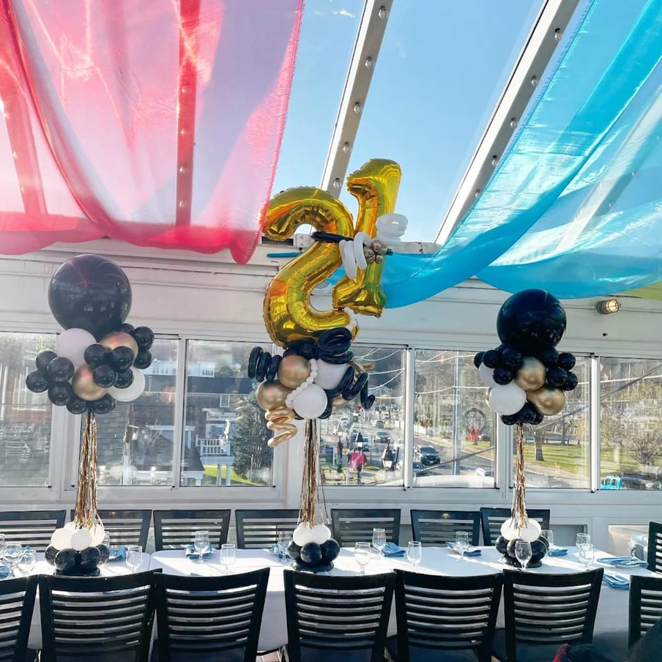 Restaurant dining room with tables set, balloon centerpieces, and red and blue drapes overhead.