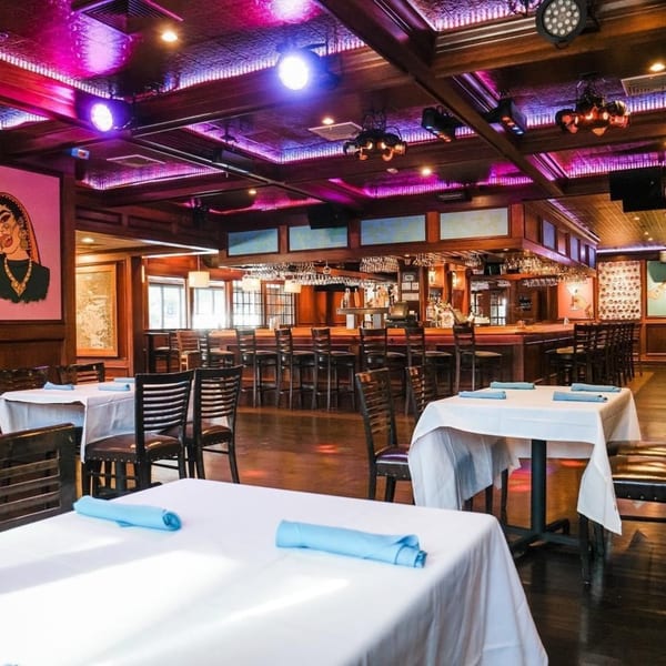Curry Club's dining room with white-clothed tables, a long bar, and purple accent lighting.