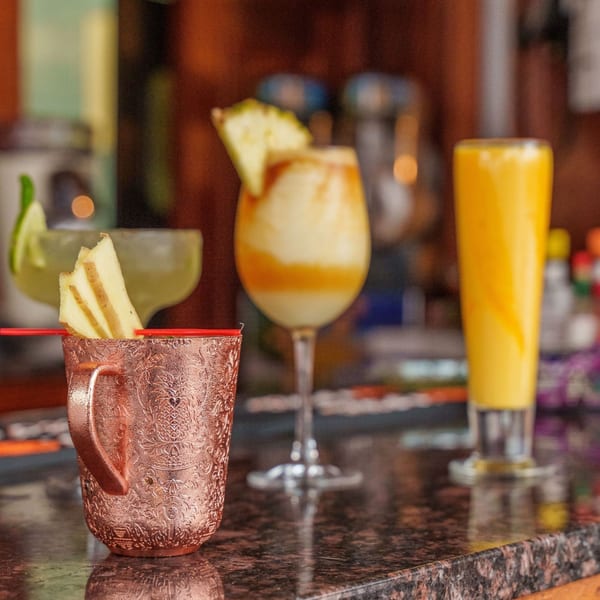 Three Indian-inspired drinks on a bar, including a copper mug and two tall glasses.