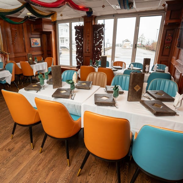 Curry Club dining room with set tables, orange and teal chairs, and large windows.