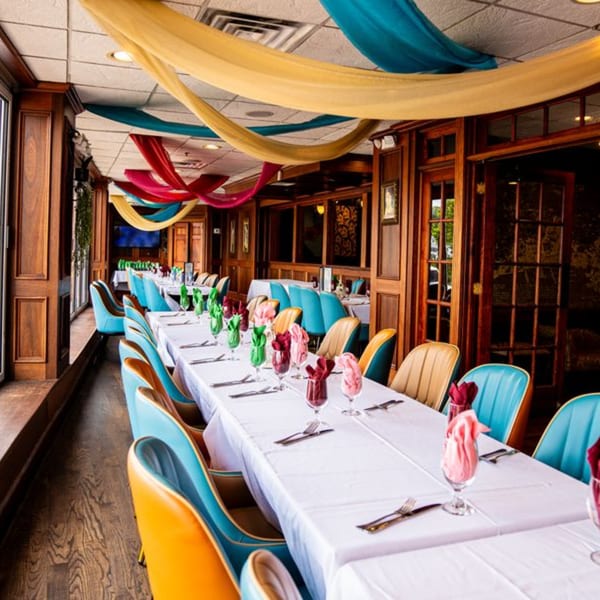 Long dining tables with colorful chairs and draped fabrics on the ceiling at Curry Club restaurant.