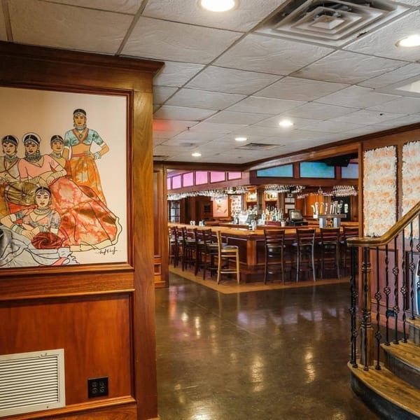 A painting of Indian women in traditional attire next to a wooden bar area with stools.