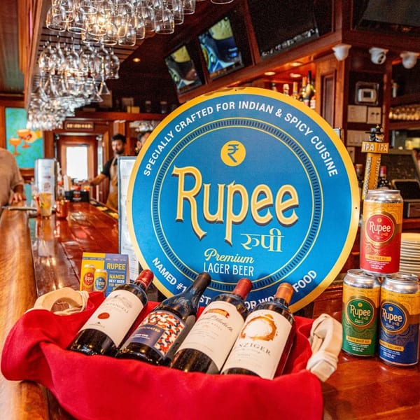 Rupee beer sign, cans, and wine bottles on a bar at Curry Club Indian restaurant.