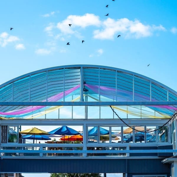Curry Club's outdoor patio with colorful umbrellas and fabric under a blue sky with birds.