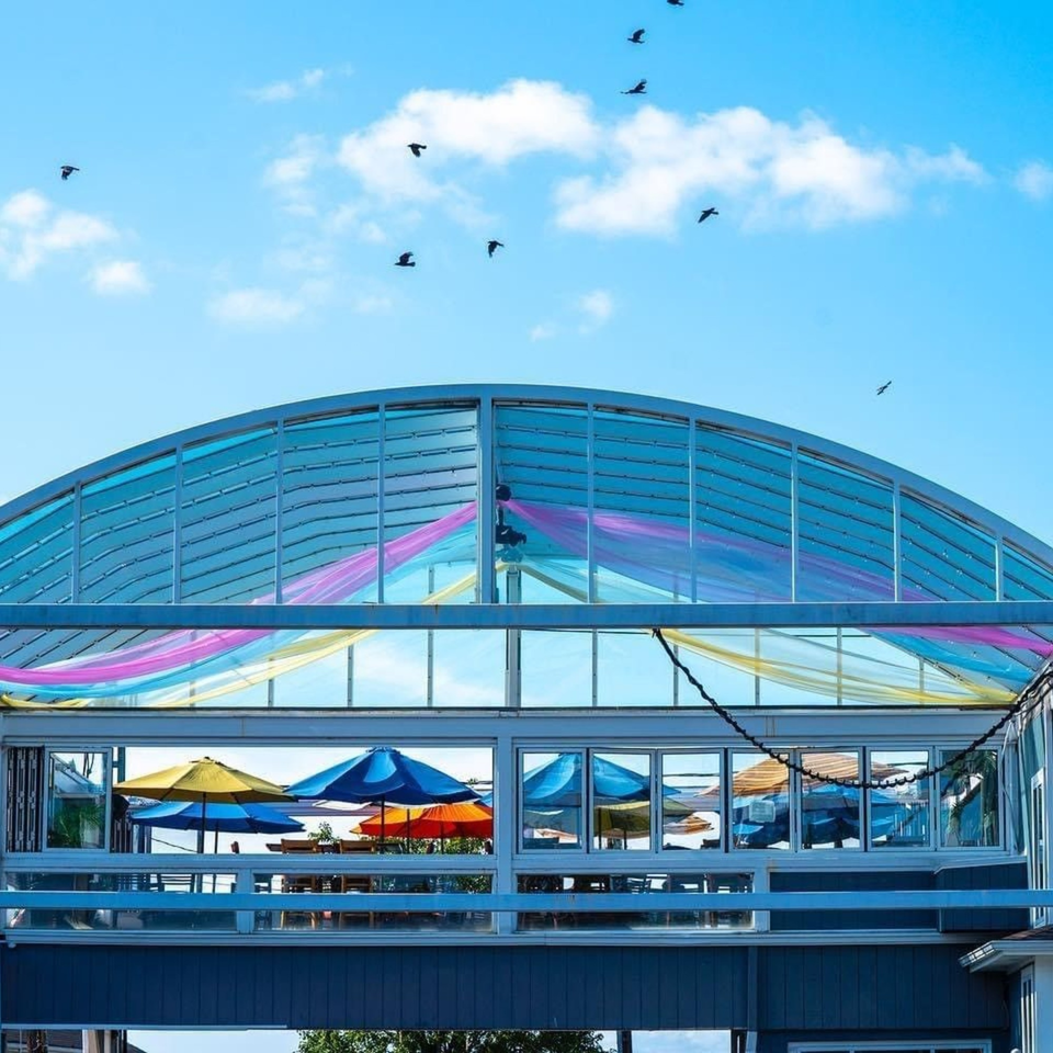 Curry Club's outdoor patio with colorful umbrellas and fabric under a blue sky with birds.