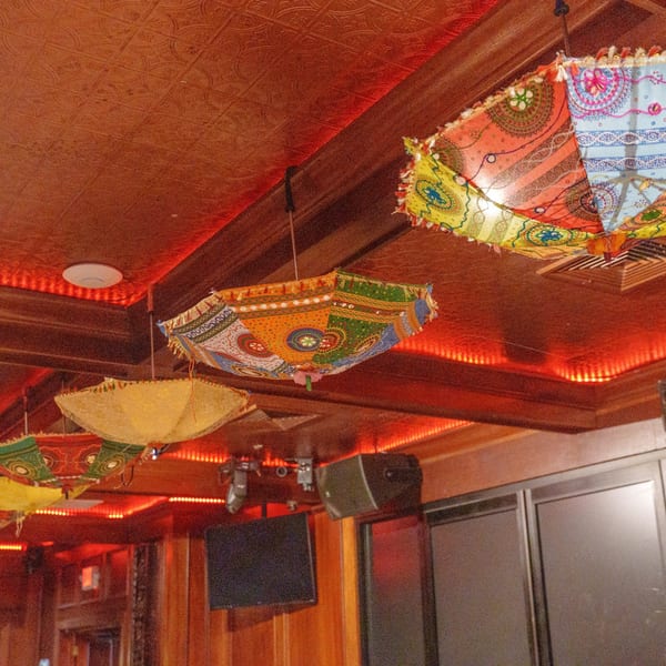 Colorful patterned umbrellas hang from the ceiling of Curry Club, illuminated by red accent lighting.