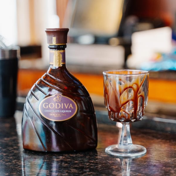 A bottle of Godiva chocolate liqueur next to a glass drizzled with chocolate syrup.